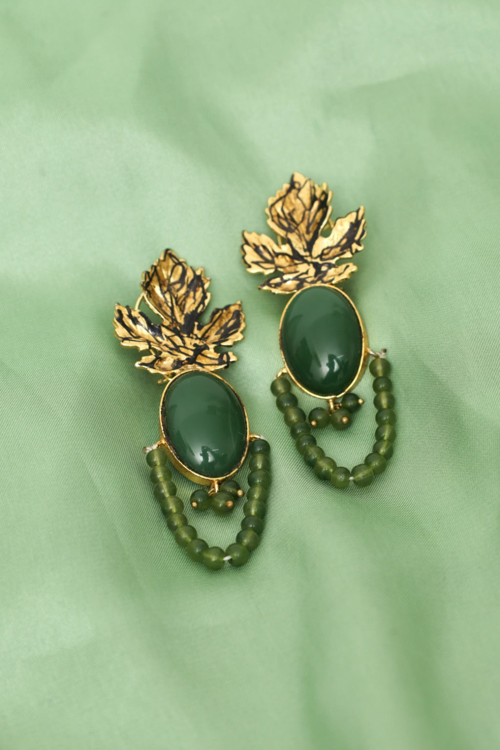 Pair of gold and green leaf-themed earrings on a green background