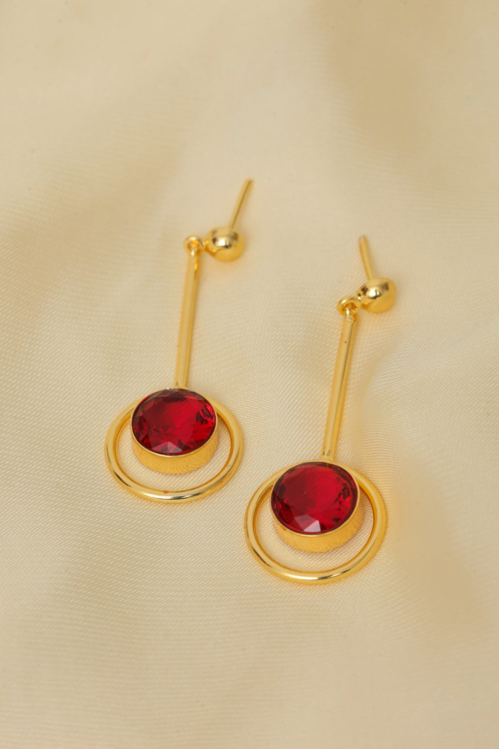 Gold earrings with red gemstones on a beige background
