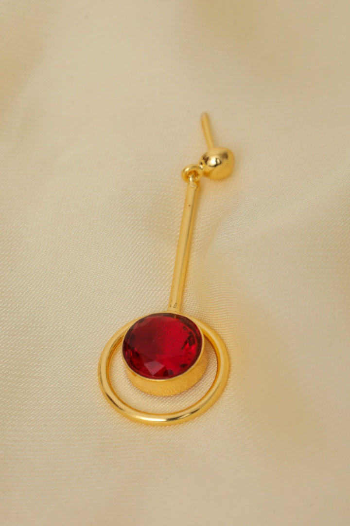 Gold earring with a red gemstone on a beige background