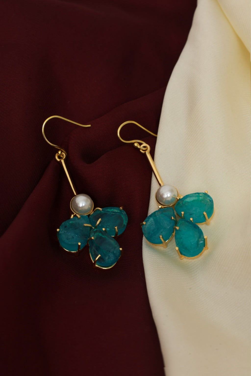 Teal earrings with gold accents and pearl centers on a fabric background