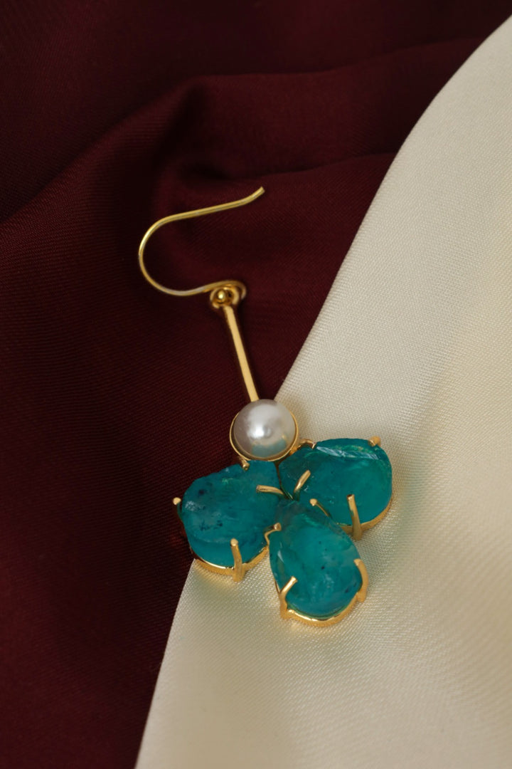 Gold earring with green leaf-like design and pearl center on a fabric background