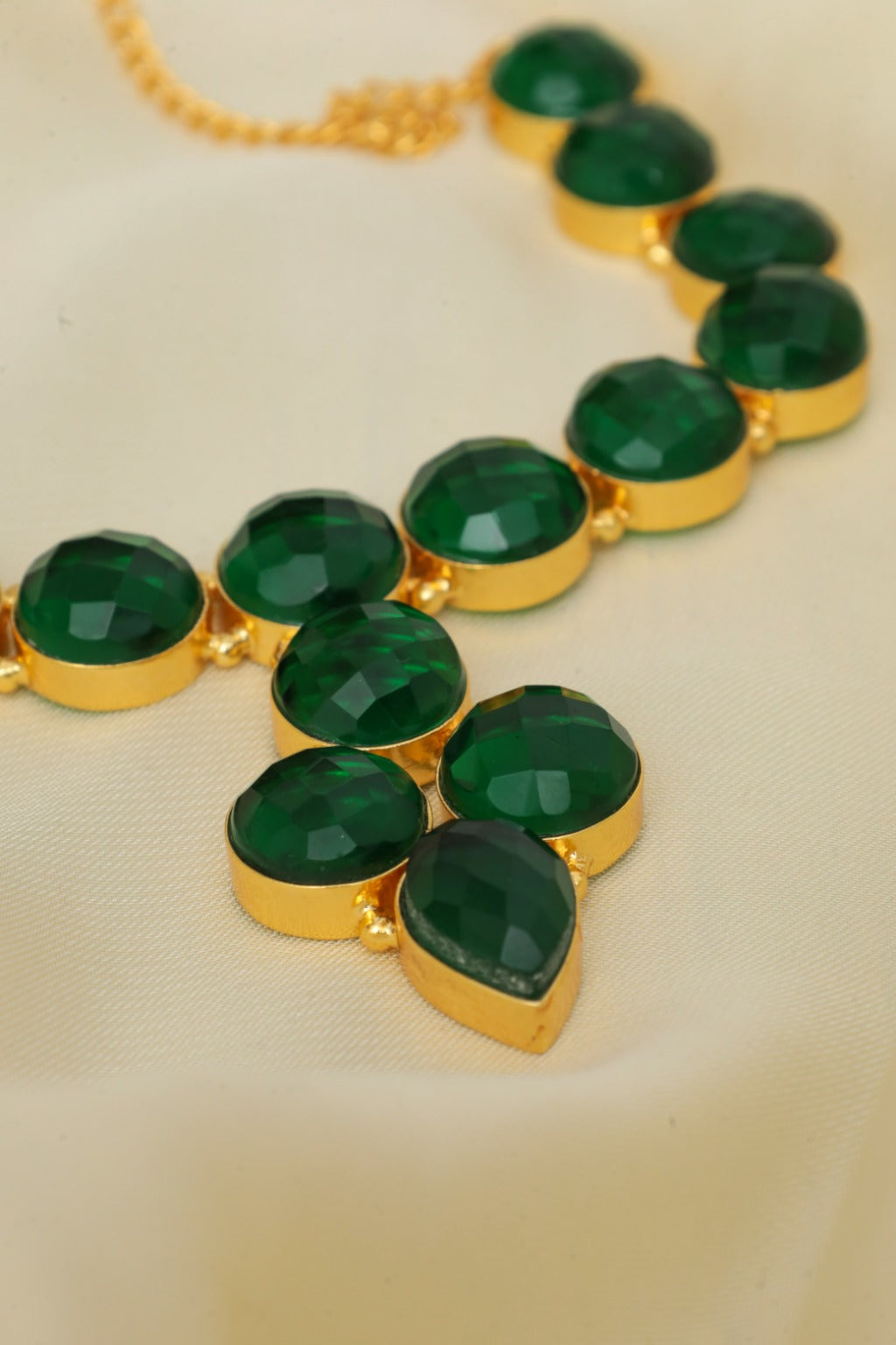 Gold necklace with green gemstones on a beige background