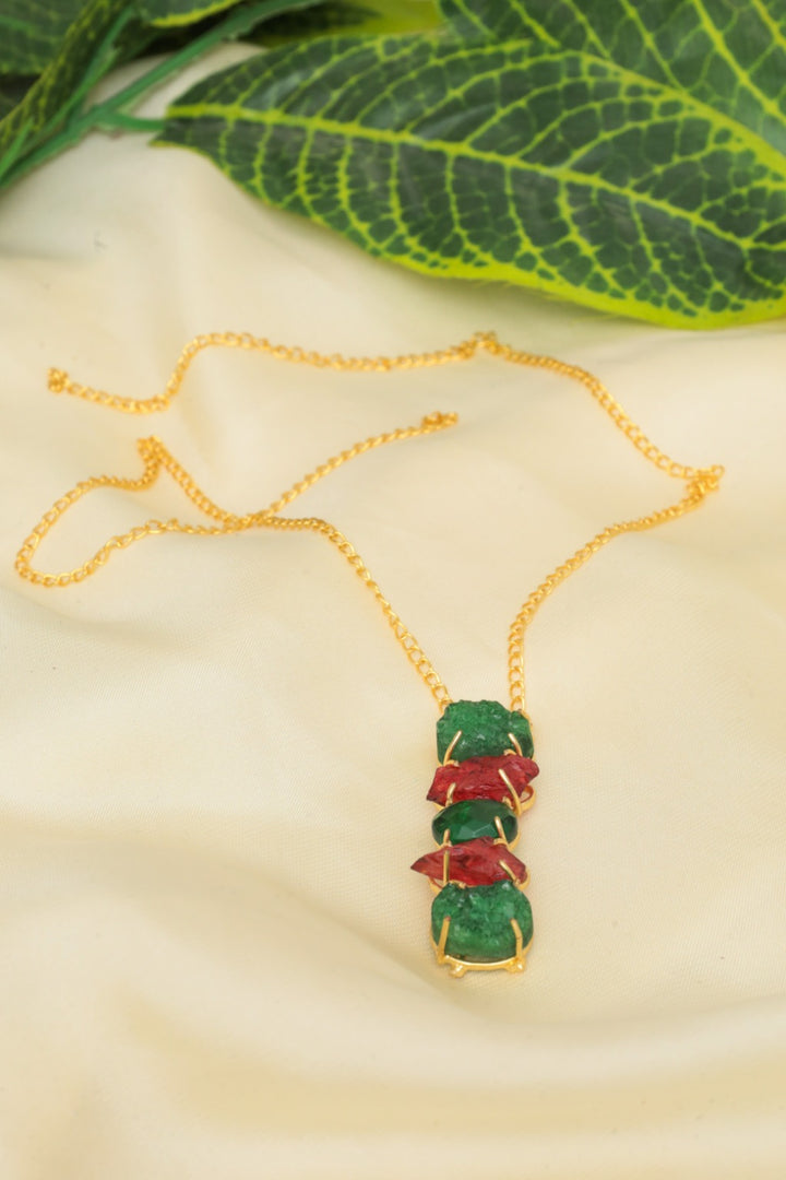 Necklace with green and red stones on a beige surface with leaves in the background