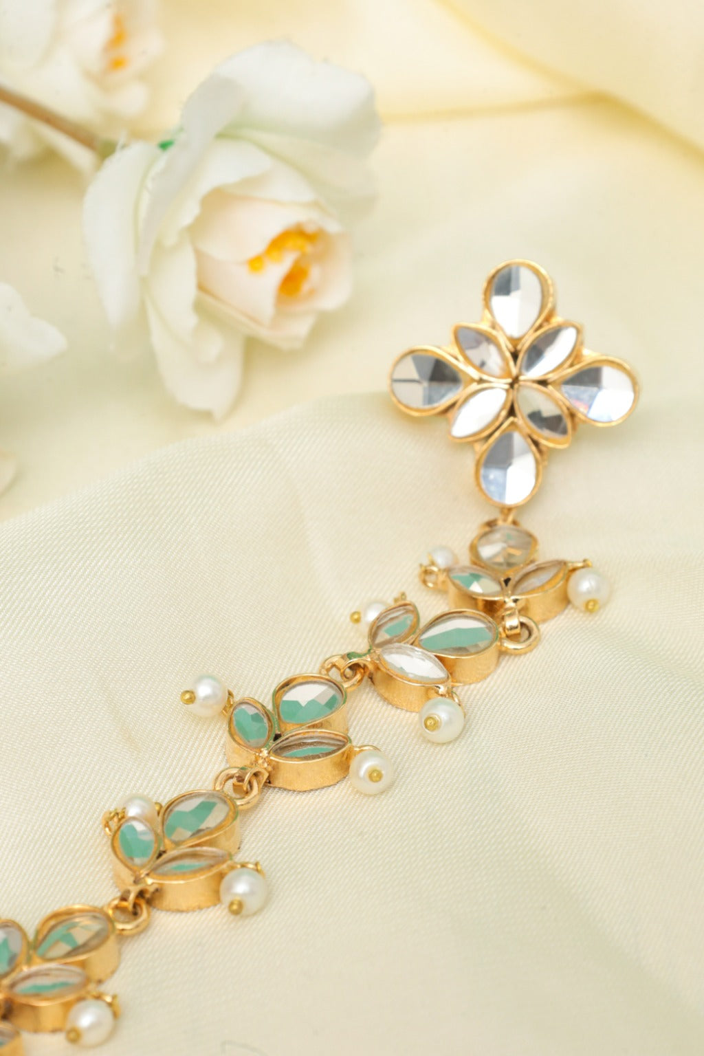 Gold bracelet with green gemstones and pearls on a light background