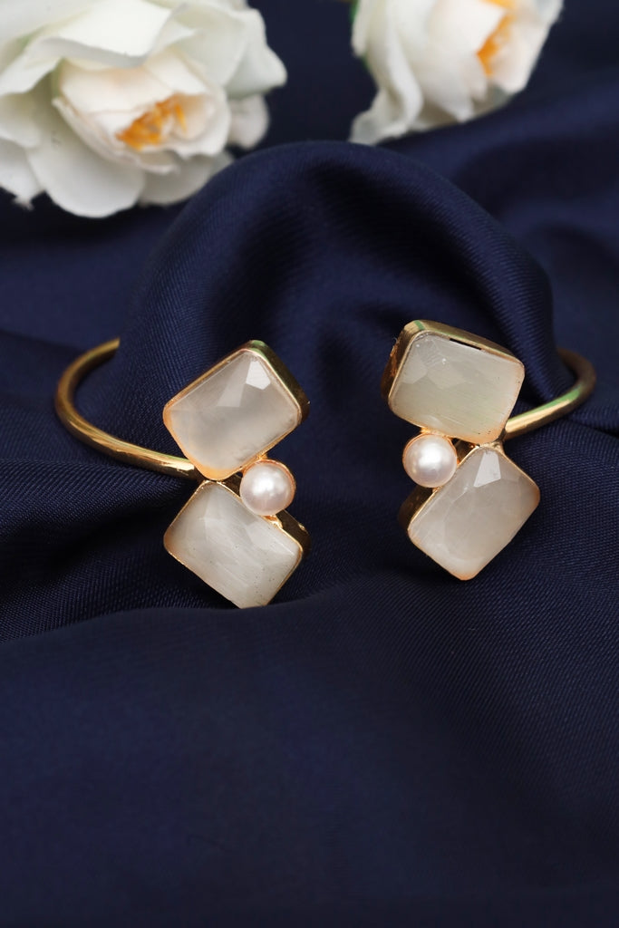 Gold and pearl bracelet on a dark blue fabric background with white flowers.