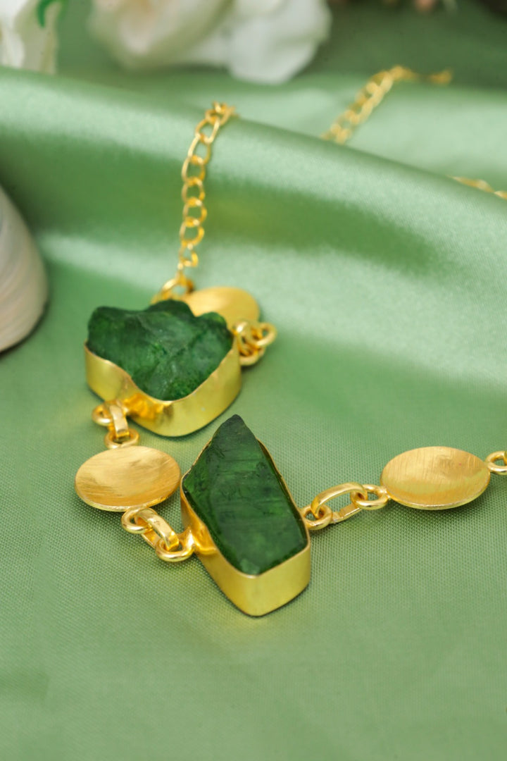 Gold necklace with green stones on a green fabric background