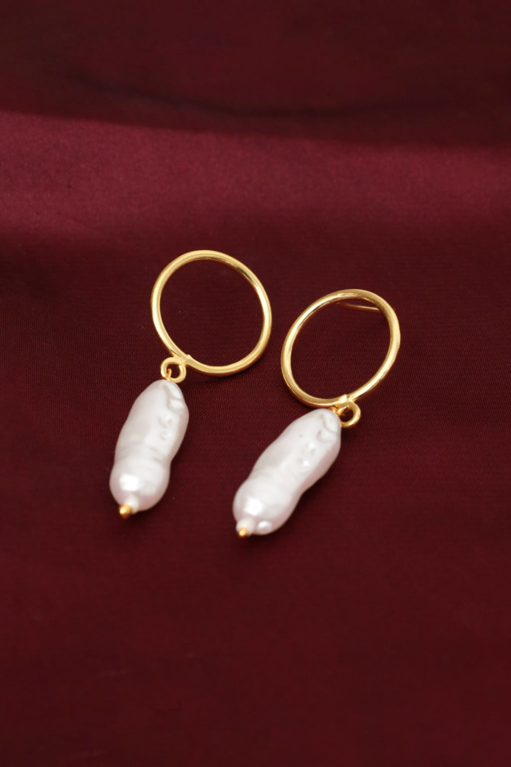 Gold hoop earrings with white pearls on a maroon fabric background