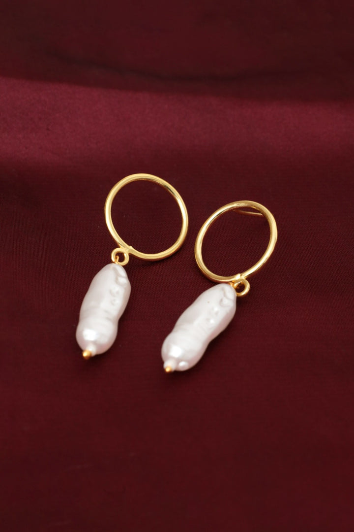 Gold hoop earrings with white pearls on a maroon fabric background