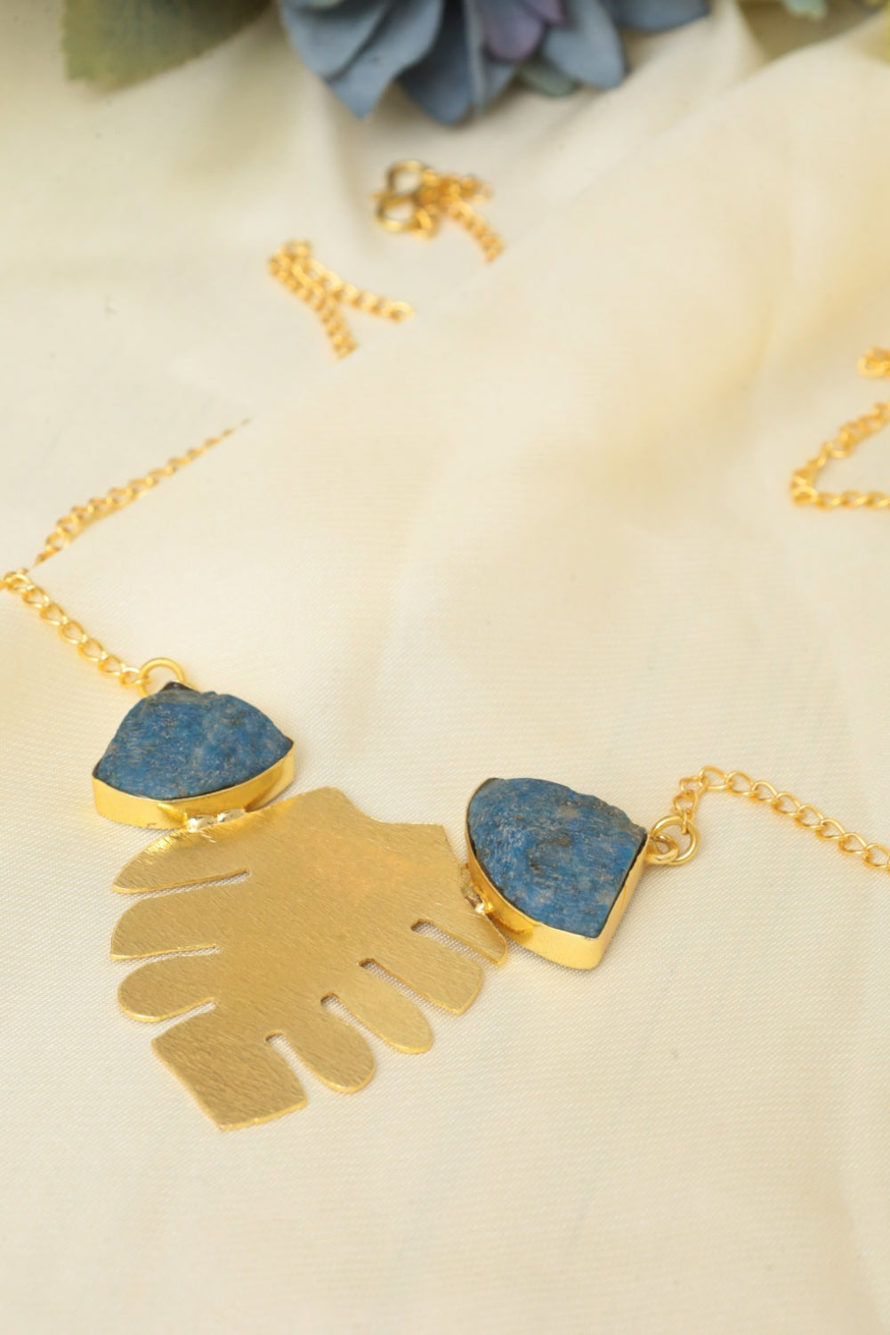 Gold necklace with blue stone pendant on a beige surface