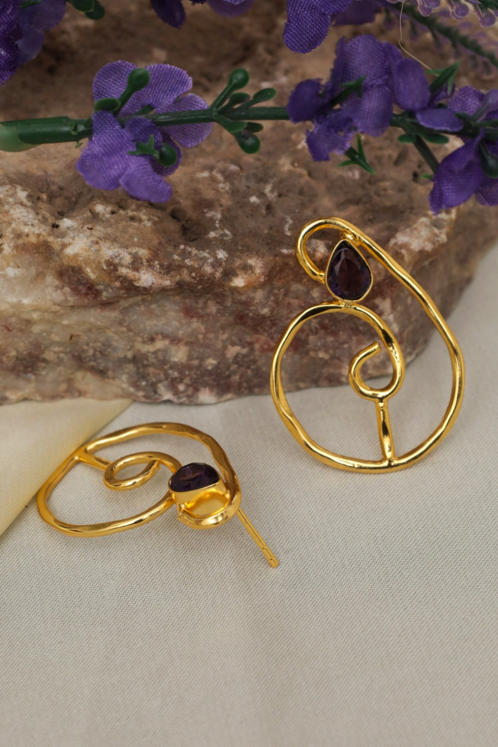 Gold earrings with purple stones on a beige fabric background