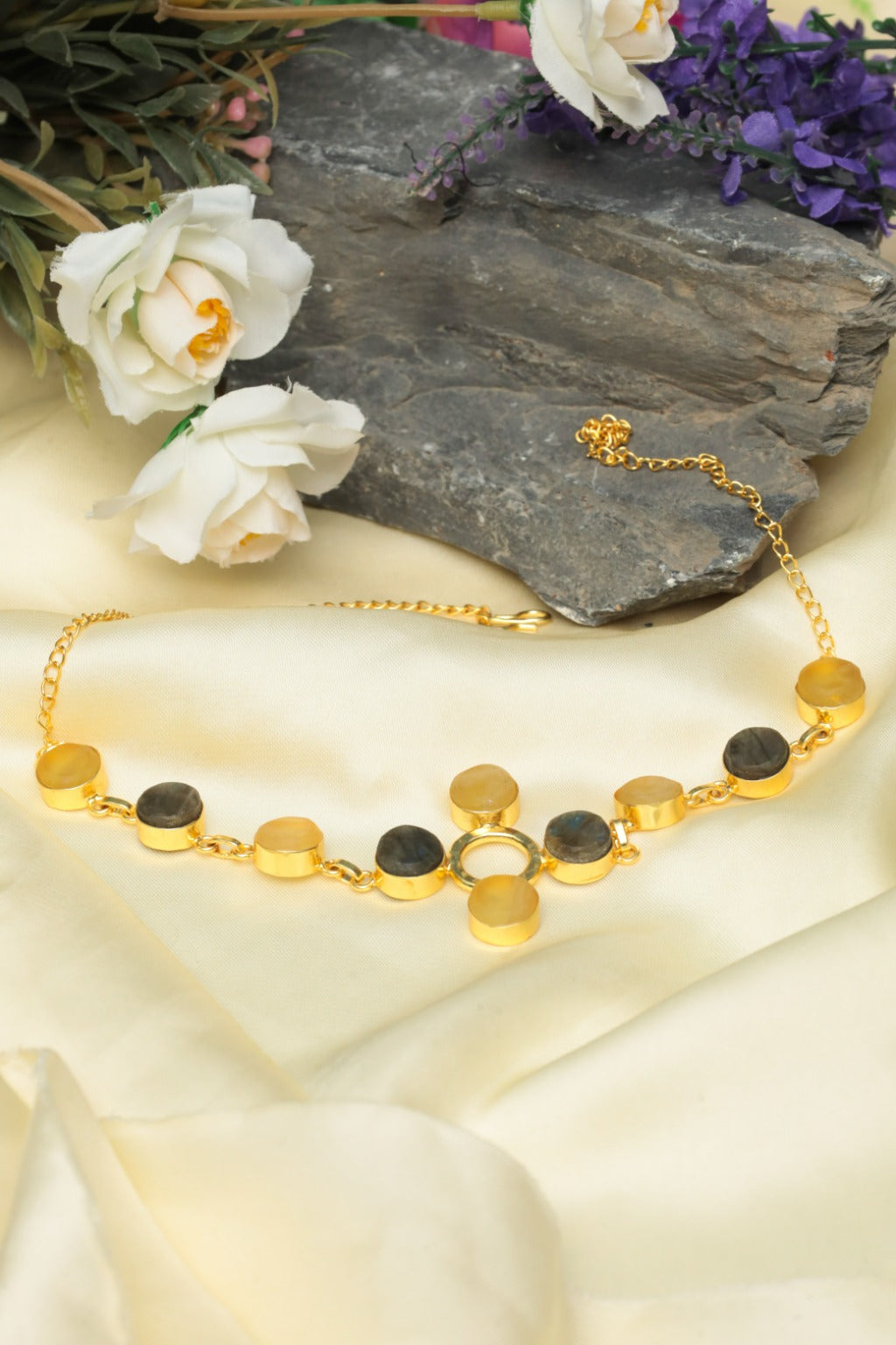 Gold necklace with black and white stones on a stone surface with flowers