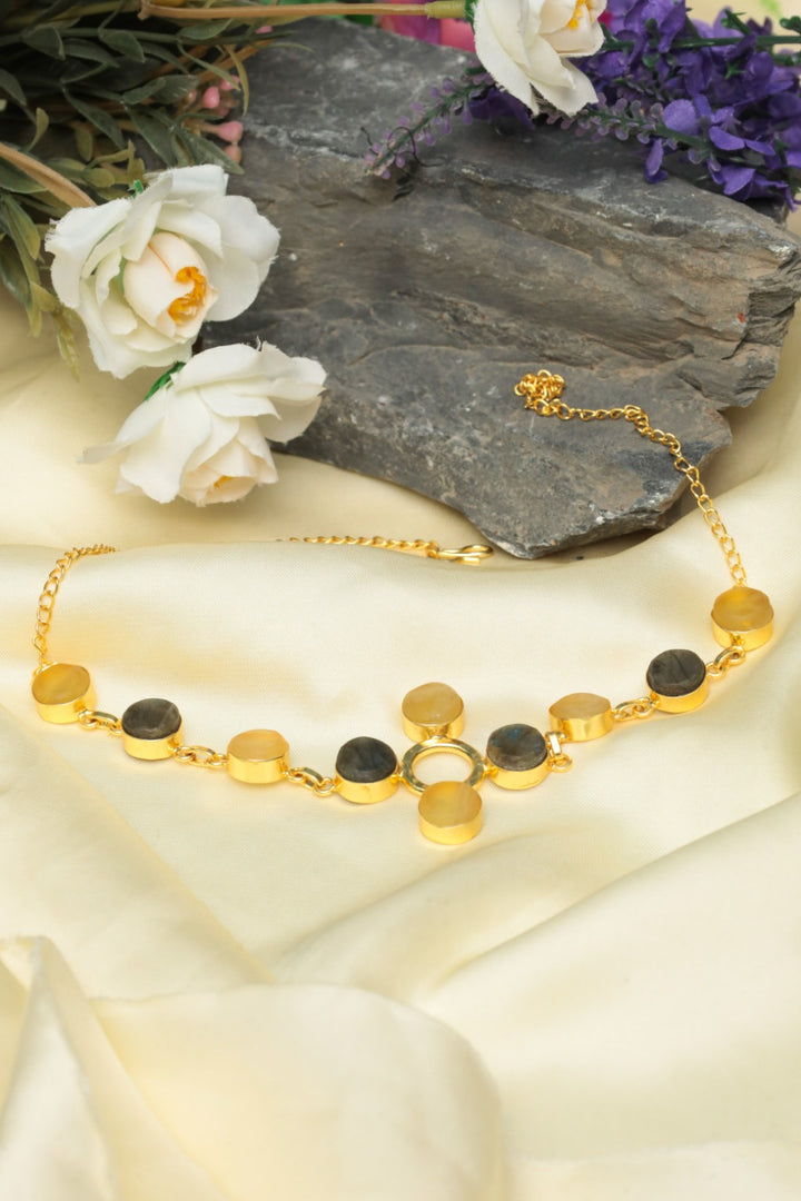 Gold necklace with black and white stones on a stone surface with flowers