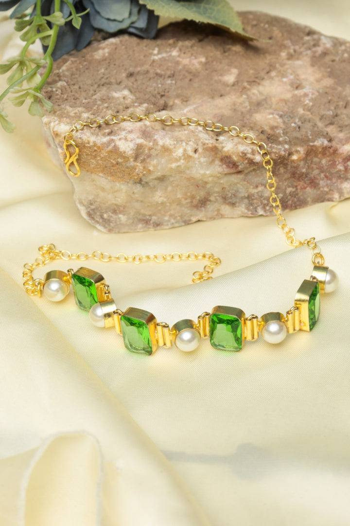 Gold bracelet with green gemstones and pearls on a stone surface