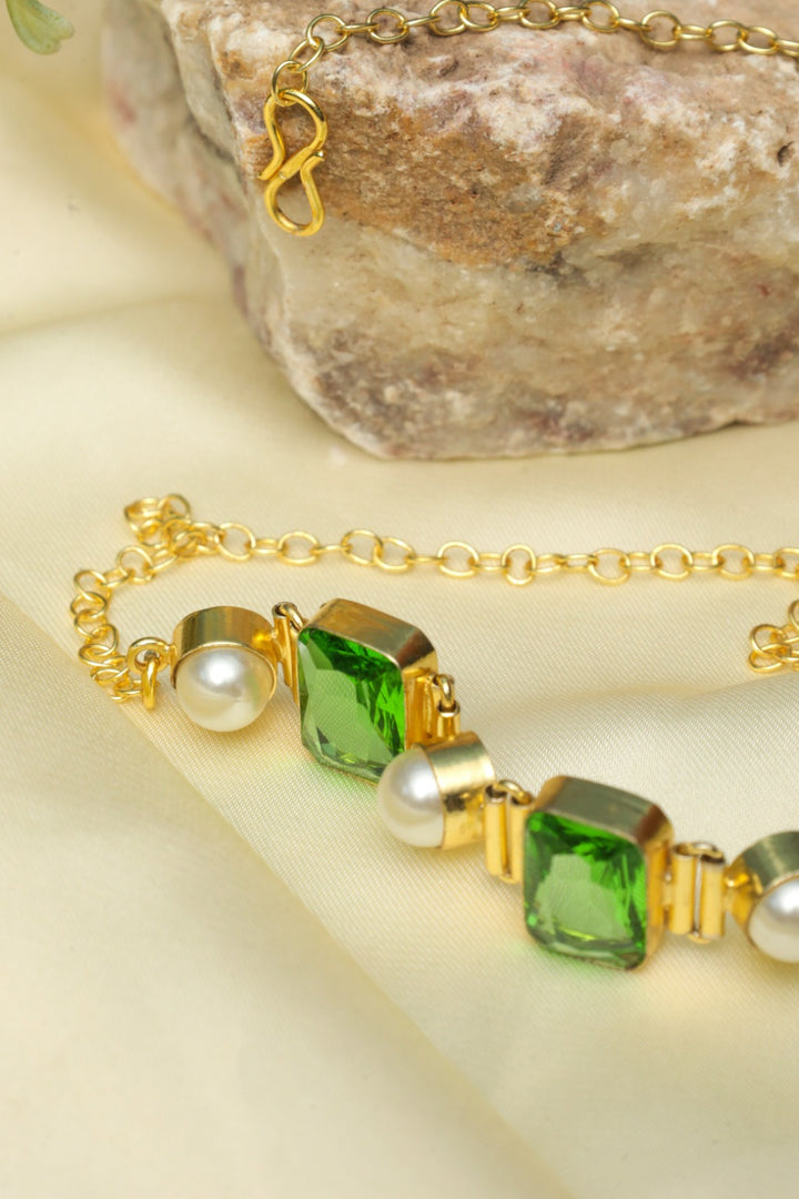 Gold bracelet with green gemstones and pearls on a stone surface