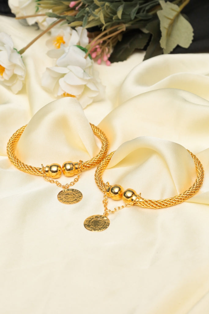 Two gold bracelets on a white fabric background with flowers.