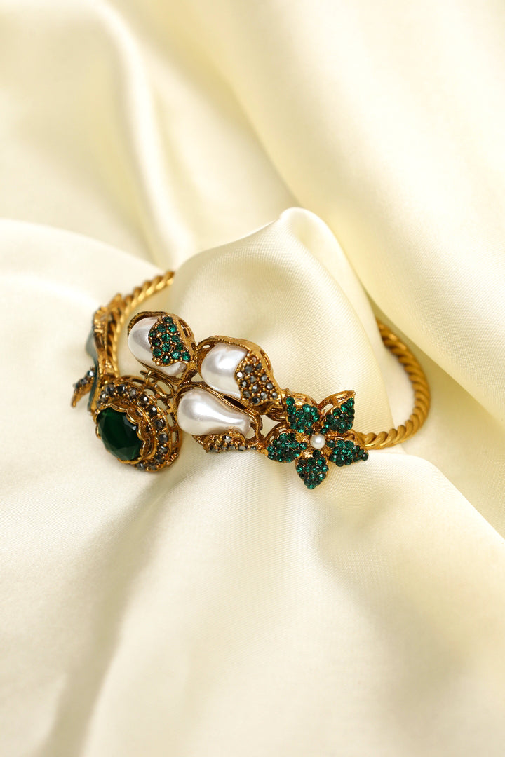 Decorative bracelet with pearls and green stones on a cream fabric background